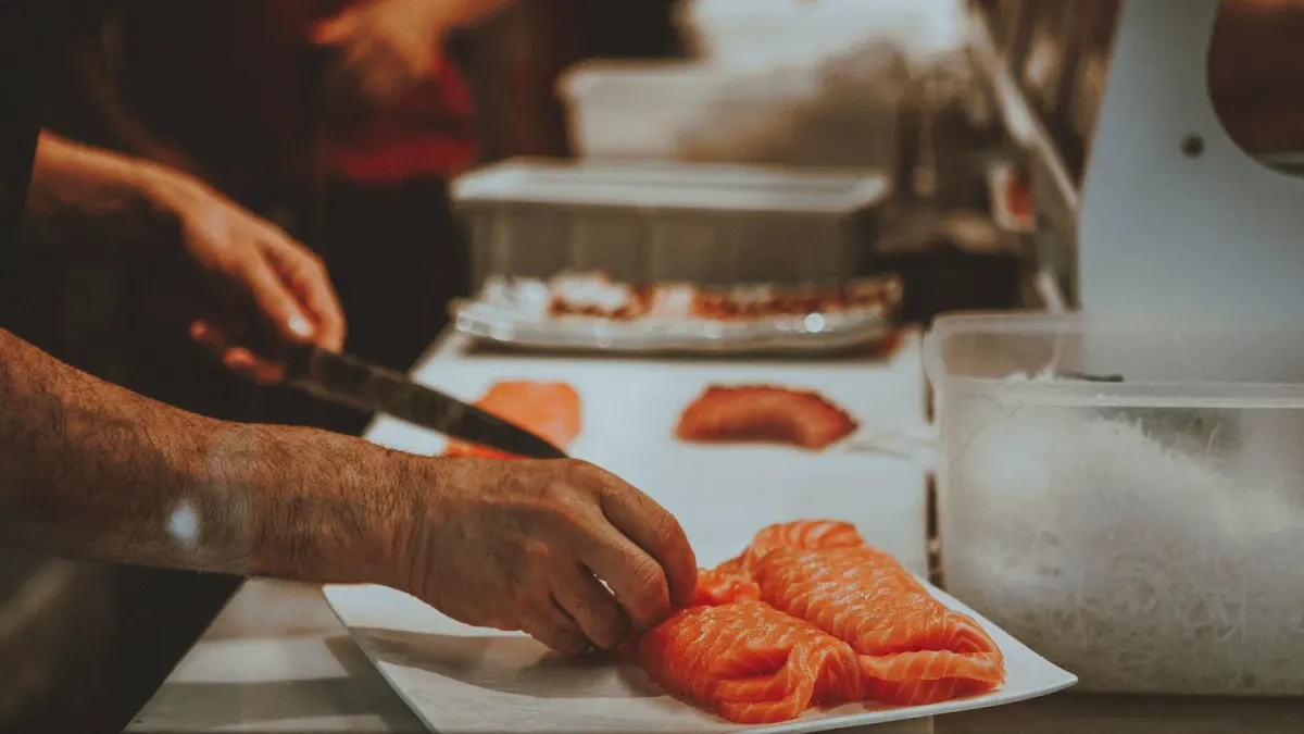 A cooked salmon fillet resting on a cutting board with a dog looking on nearby