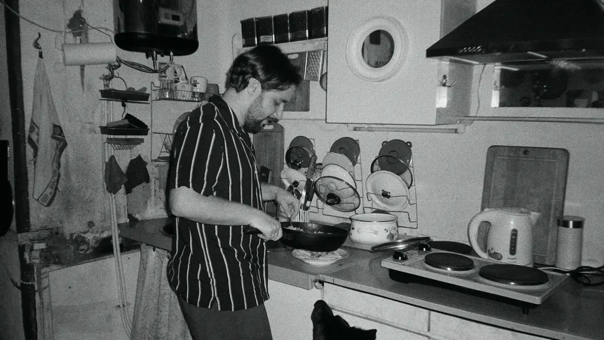 A dog eating from its bowl in a home kitchen while its owner watches nearby