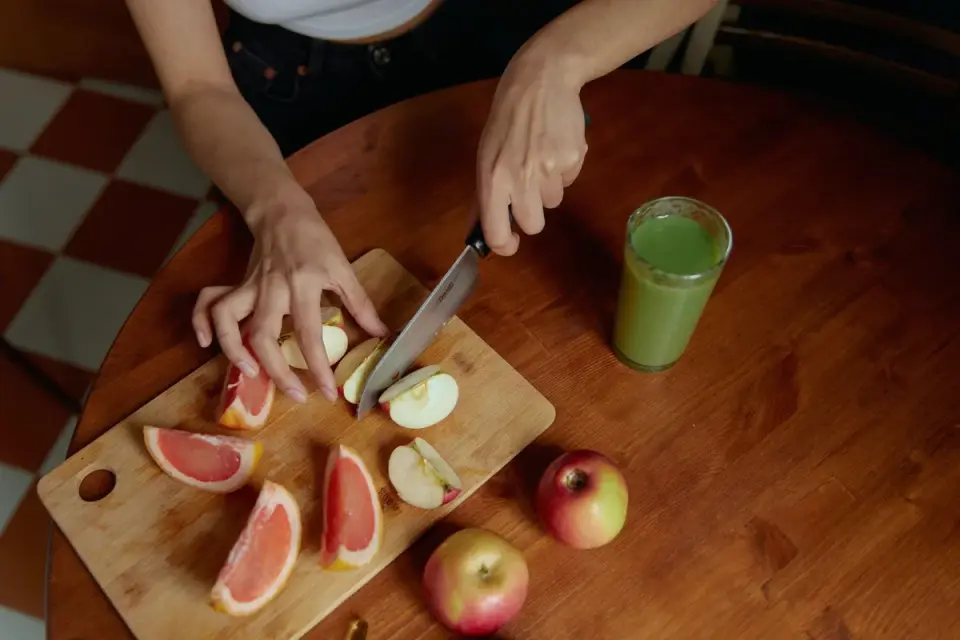 A hand slicing an apple and removing the core on a wooden cutting board