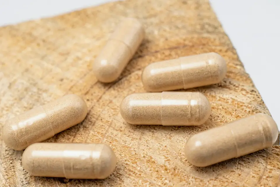 Probiotic capsules and loose powder spilled next to a supplement bottle on a wood counter